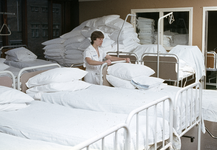 828099 Afbeelding van een leerling-verpleegkundige die ziekenhuisbedden transporteert op de beddencentrale, tijdens ...